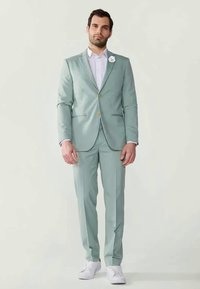 Mint green suit jacket with matching trousers, white shirt underneath, floral lapel pin, and white sneakers. Smooth fabric, tailored fit.