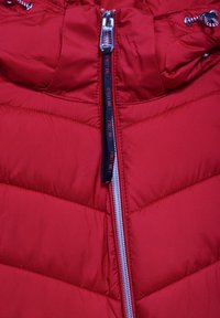 Rote Pufferjacke mit einem Reißverschluss vorne. Verfügt über eine gesteppten Textur und eine Kapuze, mit kontrastierenden Reißverschluss- und Kordelzügen Akzenten.