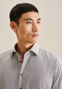 Lichtgrijs button-up shirt met een gemarmerd patroon, liggende kraag en contrasterende knopen die zichtbaar zijn aan de voorkant. Gladde stofafwerking.