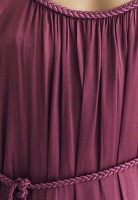 Tissu plissé violet profond avec détail de corde tressée le long du bord supérieur et ceinture en corde tressée nouée à la taille.