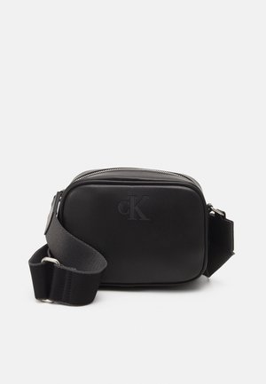 Zwarte compacte schoudertas met verstelbare brede schouderband en reliëf "cK" logo aan de voorkant, met een hoofdcompartiment voorzien van rits.