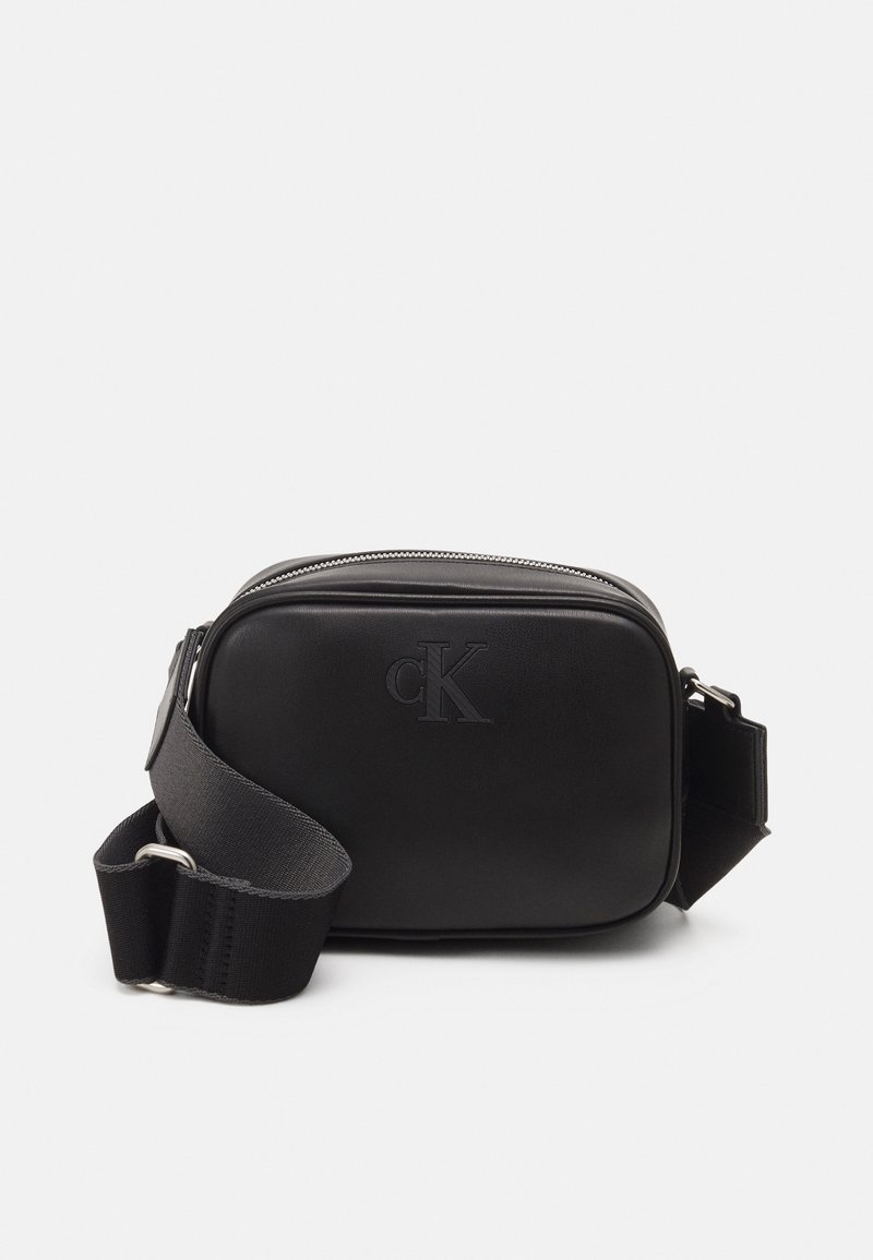 Černá kompaktní krosbody taška s nastavitelným širokým popruhem a embosovaným logem "cK" vpředu, hlavní přihrádka na zip.