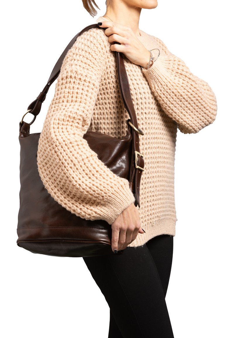 Borsa a spalla in pelle marrone con una texture liscia, dotata di una tracolla ampia e di hardware in metallo. Indossata da una persona in un maglione beige.