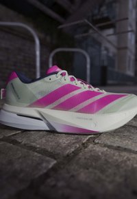 Lysegrå og lys pink løbesko med mesh-overdel og tyk hvid sål på brostensbelagt jord i urbant miljø.
