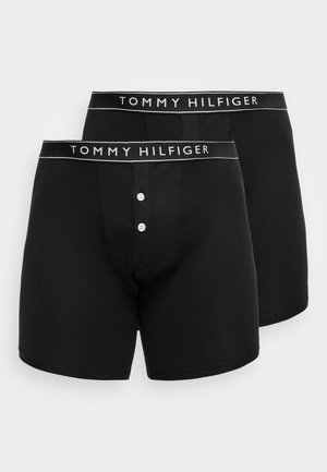 Δύο μαύρα μποξεράκια Tommy Hilfiger με λαστιχένιες μέσης με λογότυπο και κουμπωτή μπροστινή π fly, παρουσιάζονται σε λευκό φόντο.