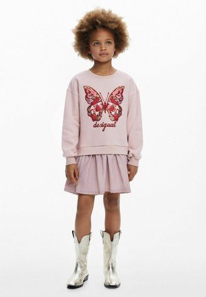Felpa rosa chiaro con una grande grafica di farfalla rossa e rosa e testo "desigual", abbinata a una gonna a strati rosa chiaro e stivali metallici argento.