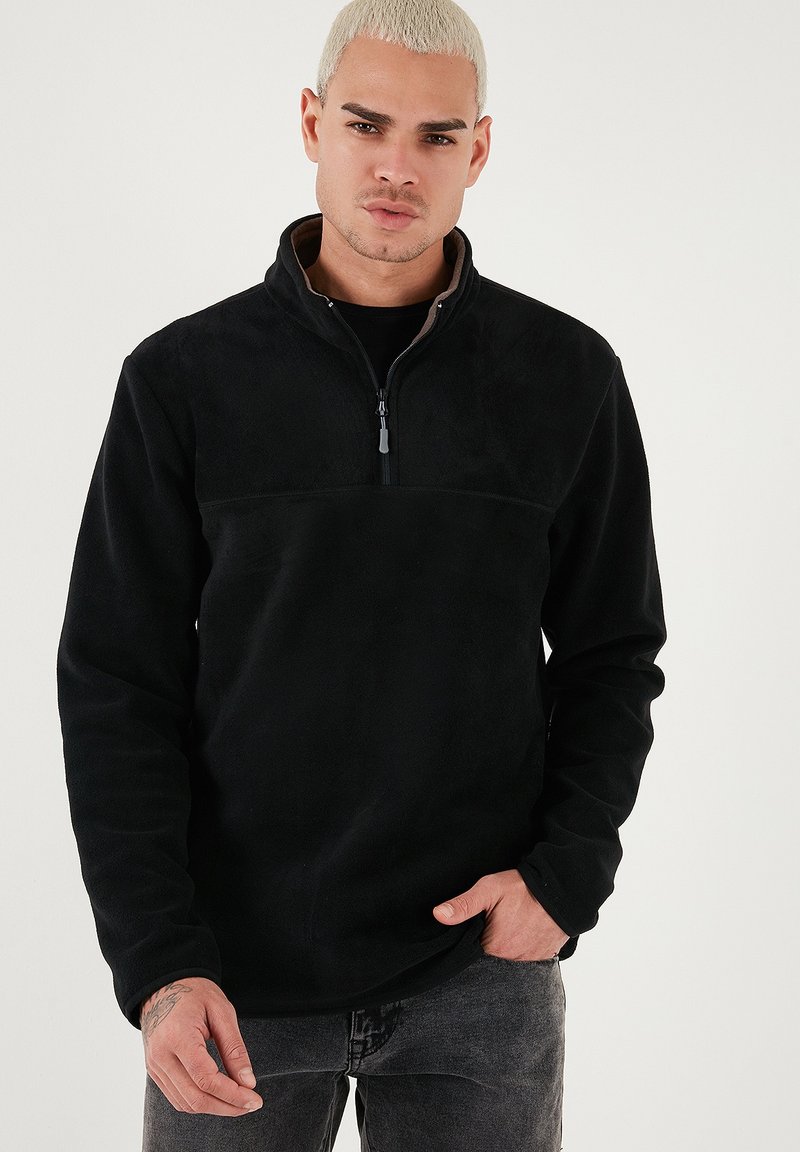 Pullover in pile nero con mezza zip e fodera a contrasto color beige. Tessuto morbido, maniche lunghe e vestibilità rilassata. Cucitura piatta distintiva sul petto.
