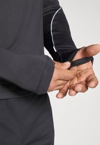 Αθλητικό μπλουζάκι με μακριά μανίκια σε μαύρο ύφασμα με υφή. Διαθέτει θηλιά για τον αντίχειρα για επιπλέον κάλυψη στον καρπό.