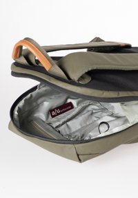 Borsa verde oliva con una patta nera, dotata di chiusura con zip. L'interno è argentato e presenta scomparti e un'etichetta del marchio. Accenti in cuoio marrone.