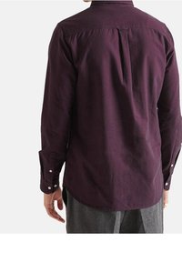 Camicia bordeaux a maniche lunghe con dettaglio sulla schiena e polsini abbottonati, realizzata in un tessuto morbido con una texture liscia.