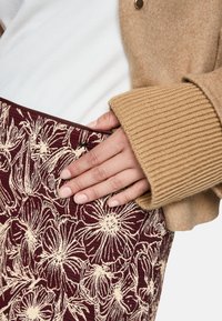 Knitted skirt with a maroon floral pattern on a textured fabric, paired with a light sweater and a tan cardigan featuring ribbed cuffs.