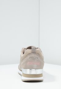 Scarpa atletica Skechers in suede beige chiaro con dettagli in rete, logo rosa sul tallone e clip metallica argentata.