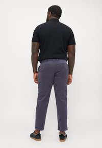 Schwarzes Polohemd für Herren kombiniert mit schmal geschnittenen, helllila Hosen und schwarzen Low-Top-Schuhen. Das Outfit zeichnet sich durch ein klassisches Design und eine glatte Textur aus.