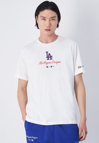 Witte katoenen t-shirt met "LA" logo en "Los Angeles Dodgers" tekst in het rood. Korte mouwen, ontspannen pasvorm. Champion logo op de linker mouw.