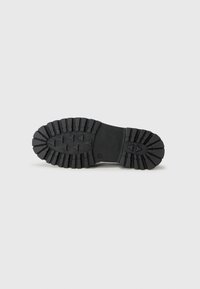 Black rubber shoe sole with thick treads and triangular patterns, designed for traction and durability. Smooth finish with no visible markings.