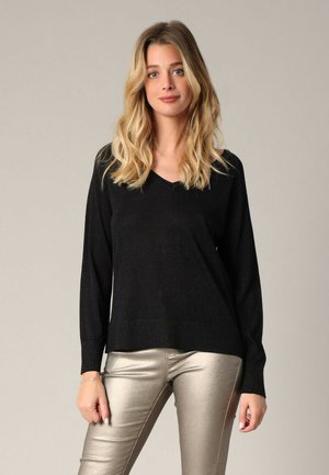 Pull noir à col en V avec des manches longues, fabriqué à partir d'un tissu texturé. Assorti à un pantalon slim en métal doré brillant.