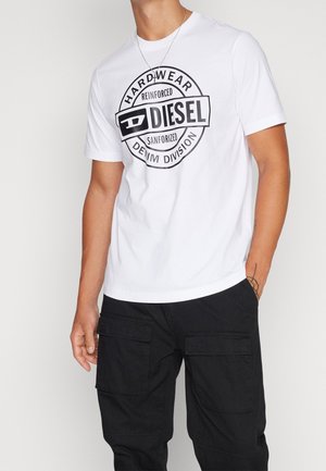 T-shirt en coton blanc avec un logo rond noir au centre, comportant le texte « DIESEL HARDWEAR REINFORCED SANFORIZED ». Manches courtes et col rond.