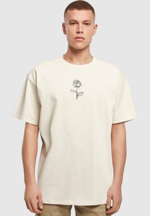 Beige oversized T-shirt lavet af bomuld, med en sort linjetegning af en rose i midten. Afslappet pasform med korte ærmer.