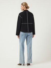 Μαύρο μπουφάν με αντίθετες λευκές ραφές, ίσια γραμμή, ψηλός γιακάς, συνδυασμένο με ανοιχτό μπλε φαρδιά παντελόνια και καφέ τακούνια.