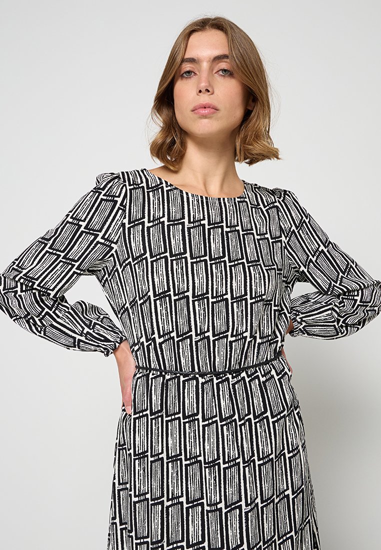 Vestido de patrón en blanco y negro con mangas largas, cuello redondo y cintura ceñida, con detalles de rayas verticales en toda la prenda.