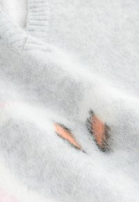 Lysegrå sweater lavet af blødt materiale, med en fnugget tekstur og et subtilt mønster med orange og pink accenter.