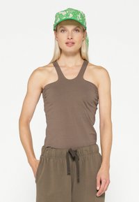 Top marrone senza maniche con scollatura a girocollo e dettagli arricciati sui lati, abbinato a pantaloni olive verdi con coulisse e un cappellino verde a strisce.