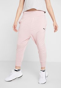 Roze joggers met een losse pasvorm, een brede tailleband, omgeslagen enkels en een klein zwart logo aan de zijkant, gecombineerd met witte sneakers.