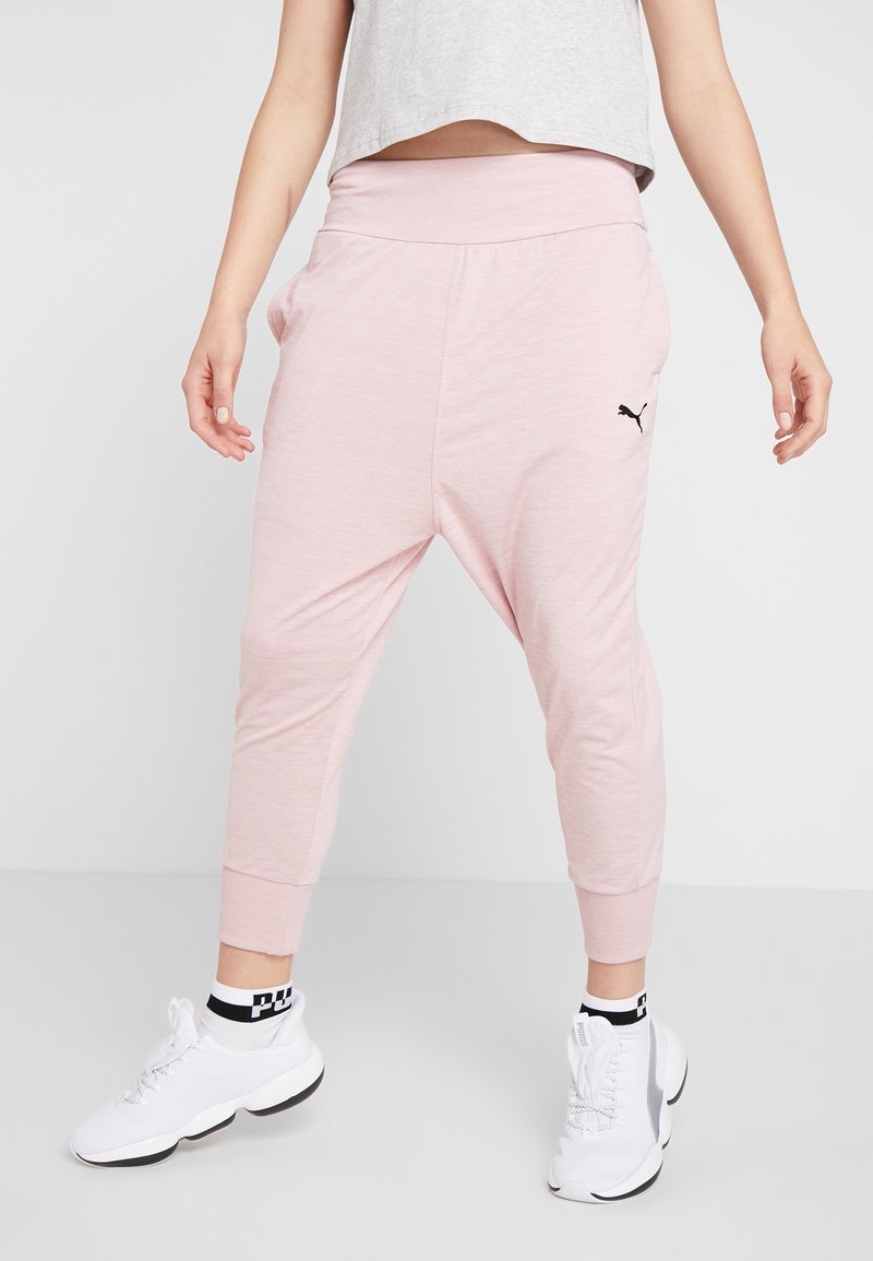 Roze joggers met een losse pasvorm, een brede tailleband, omgeslagen enkels en een klein zwart logo aan de zijkant, gecombineerd met witte sneakers.