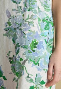 Hand resting beside fabric with large blue and green floral print on white background.