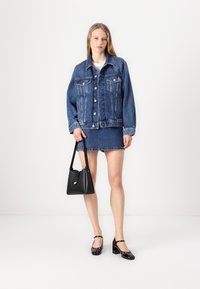 Denim jacket with large front pockets, buttons, and a relaxed fit. Paired with a denim skirt, black handbag, and patent leather shoes.