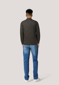 Mörkgrön ribbad stickad tröja med rund halsringning, kombinerad med ljusblå denimjeans och vita sneakers, visad bakifrån.