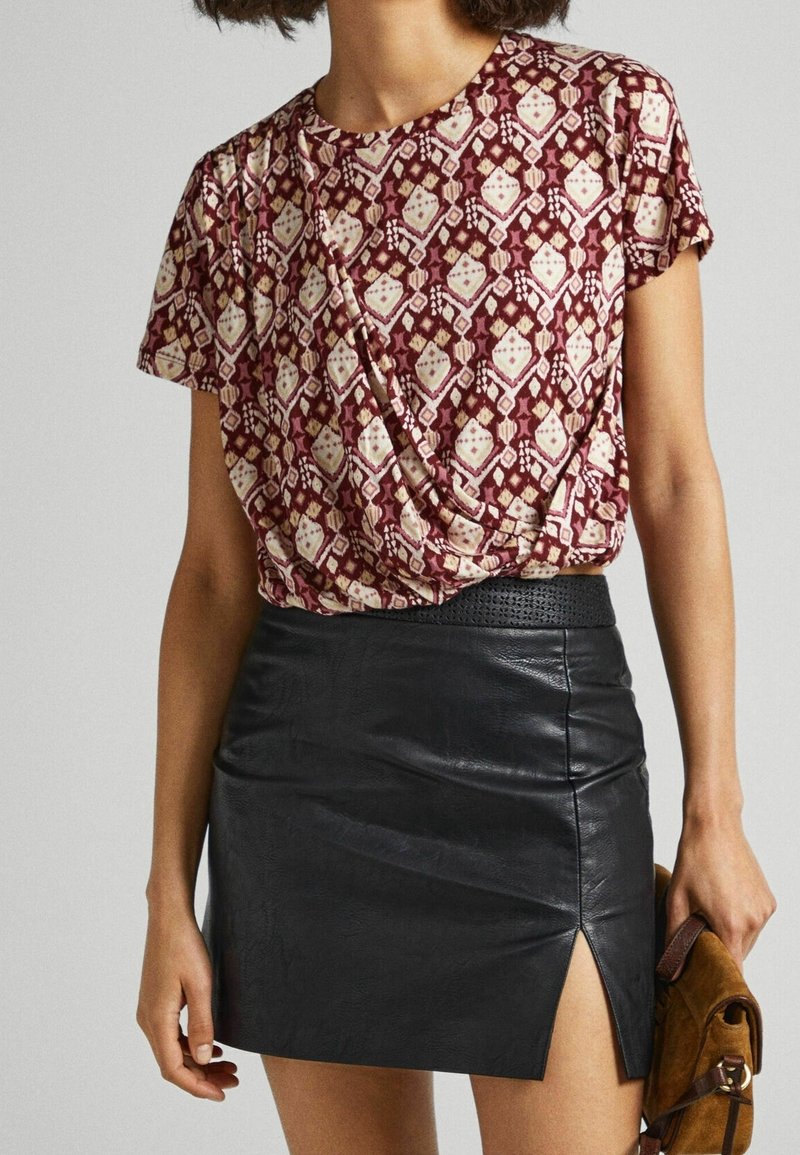 Camiseta de manga corta con un estampado rojo y crema, diseño anudado en la cintura. Falda mini de cuero negro con una abertura lateral y cinturilla texturizada.
