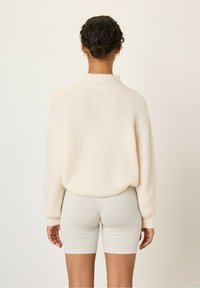 Kremasti rebrasti džemper s visokim ovratnikom i oversized krojem, uparen s svijetlosivim uskim šortsevima. Mekana tekstura, minimalistički dizajn, bez vidljivih uzoraka.