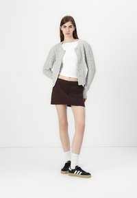 Light gray knitted cardigan with cable pattern, white cropped top, dark brown pinstriped skirt, white socks, and black sneakers with three stripes.