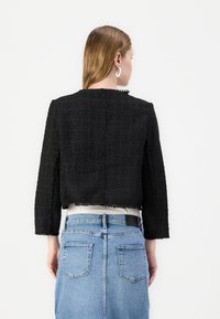 Sort tweedjakke med et kort design, teksturert stoff og frynset kanter. Kombinert med et lys blått denimskjørt med baklommer.