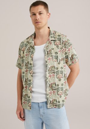 Chemise à manches courtes avec boutons en tissu texturé. Fond vert avec des motifs floraux et des tigres en rouge et noir. Design à col ouvert.