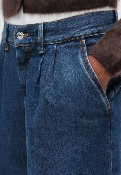 Pantalones de mezclilla con un tono azul oscuro, con cintura alta, frente plisado y costuras visibles. Incluyen bolsillos laterales y cierre de botón.