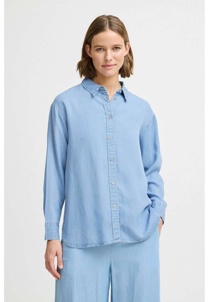 Camisa de denim de manga larga en azul claro, con botones en la parte frontal, cuello y corte relajado. Textura suave y detalles de costura sutiles.