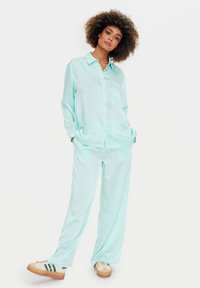 Set da casa in seta di colore azzurro chiaro, composto da una camicia con bottoni e taschino e pantaloni larghi, abbinato a sneaker beige.