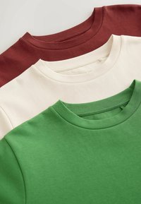 Trois t-shirts à col rond pliés en vert, blanc cassé et rouge foncé, disposés en pile avec un chevauchement sur une surface claire.
