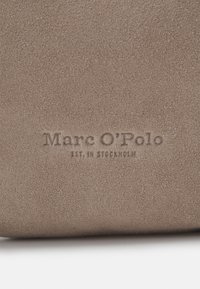 Hnědá semišová látka s jemnou strukturou a vyraženým textem "Marc O'Polo Est. in Stockholm". Jednoduchý, čistý design bez dalších detailů.