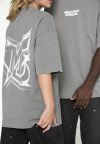 Szare, duże t-shirty z logo z przodu i dużą grafiką na plecach. Wykonane są z miękkiego materiału, mają krótkie rękawy.