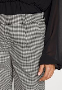 Pantalons à motif pied-de-poule noir et blanc avec une coupe droite et des détails de poche subtils, associés à un haut noir fluide.