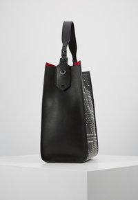 Czarna skórzana torebka o strukturalnym kształcie, z czerwonym wnętrzem i dekoracyjnymi białymi wzorami po bokach. Dołączony regulowany pasek.