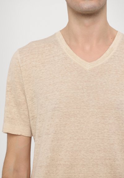 Beige V-Ausschnitt-T-Shirt aus leichtem, leicht strukturiertem Stoff, mit kurzen Ärmeln und lockerer Passform. Minimale Nähte sichtbar.