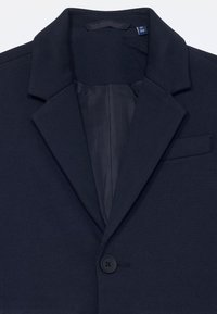 Blazer navy en tissu lisse avec col cranté, fermeture à un bouton et un détail de poche subtil sur le côté gauche.