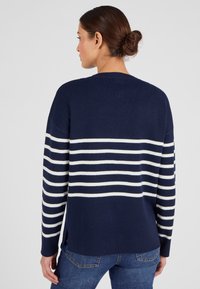 Maglione a maglia blu navy con ampie strisce orizzontali bianche. Presenta una vestibilità rilassata, scollo rotondo e spacchi laterali sull'orlo.