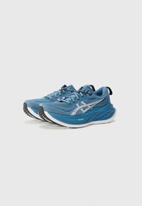 Blue athletic shoes with mesh upper, laces, and distinctive logo. Thick white midsole with textured outsole for traction.