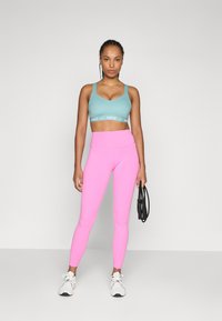 Sportbehå i ljusblått med en logoband, kombinerat med högmidjade, tighta rosa tights. Modellen håller i ett svart hopprep. Vita sneakers.