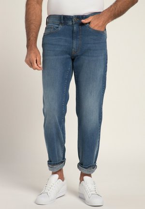 Jeans en denim bleu avec une coupe droite, un léger délavage et des ourlets retroussés. Assortis à des baskets blanches, ils présentent des poches avant et une fermeture à bouton.